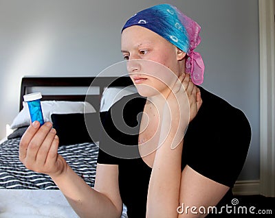 Portrait of a young cancer patient in a headscarf looks at bottle of pills with concern Stock Photo