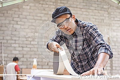 Young carpenter applying wood vinyl into a furniture Stock Photo