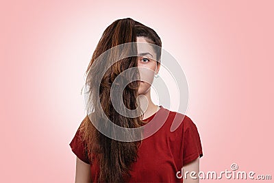 Portrait of a young Caucasian woman with a ponytail covering half of her face. Pink background. The concept of unruly hair and its Stock Photo