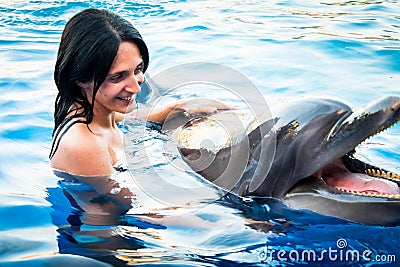 Portrait of young Caucasian woman smile with dolphin in pool water of Batumi delphinarium. Swim with dolphin experience concept Stock Photo