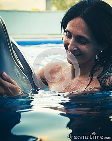 Portrait of young Caucasian woman smile with dolphin in pool water of Batumi delphinarium. Swim with dolphin experience concept Stock Photo