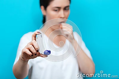 Portrait of a young coughing woman showing an inhaler. Background is blurred. Hand in focus Stock Photo