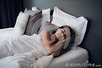 Portrait of a young cute brunette girl sleeping on a bed in light livingroom. Her head is on grey pillow and she is Stock Photo