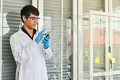 Portrait of young doctor scientist wearing safty glasses and blue rubber gloves using mobile smartphone in working laboratory room Stock Photo