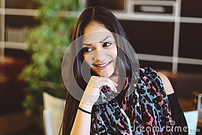 Portrait of young dreaming girl in cafe. Beautiful girl sits in coffee shop and looks,Girl smiling, hand near face Stock Photo