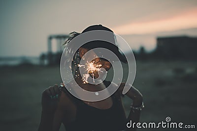 Portrait of young european girl holding sparkle stick under the patio outdoor. Happy smiling woman celebrating with fireworks Stock Photo