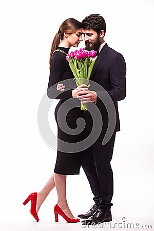 Portrait of young family couple in love with bouquet of lila tulips posing dressed in classic clothes on white backround. Stock Photo