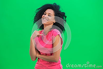 Portrait of young female African American flirtatious smiling. Black woman with curly hair in pink tshirt poses on green Stock Photo