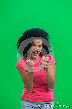 Portrait of young female African American is texting on phone and rejoice good news. Black woman with curly hair in pink Stock Photo