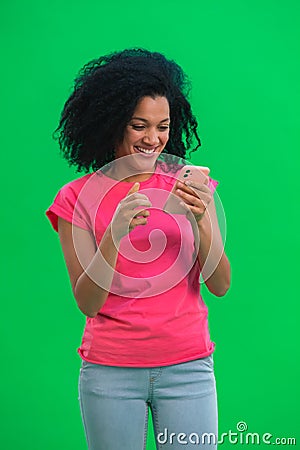 Portrait of young female African American is texting on phone and rejoice good news. Black woman with curly hair in pink Stock Photo
