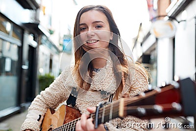 Portrait Of Young Female Musician Busking Playing Acoustic Guitar And Singing Outdoors In Street Stock Photo