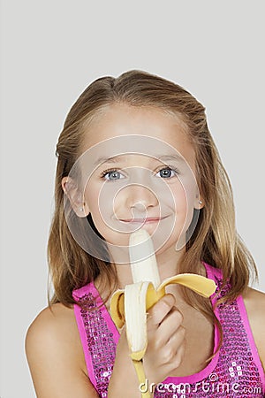 Portrait of young girl holding banana against gray background Stock Photo