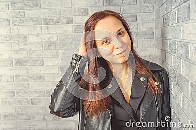 Portrait of a young girl without makeup on her face in a black jacket against a gray brick wall. Stock Photo