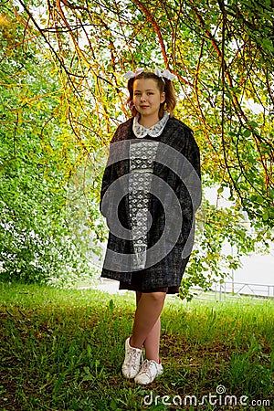 Portrait of a young girl in an old school uniform of the USSR with a black dress and a white apron. Teenager in the Park among the Stock Photo