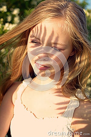 Portrait of a young girl in the shade of palm leaves. The shadow of the leaves falls on her face. Summer concept Stock Photo