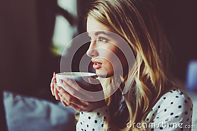 Portrait of young gorgeous female drinking tea and thoughtfully looking out of the coffee shop window while enjoying her leisure t Stock Photo