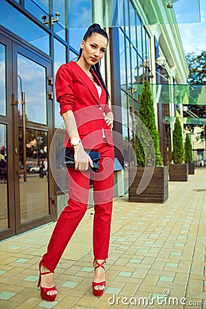 Portrait of young gorgeous lady with high pony tail in red costume and high-heeled shoes standing in front of mirrored shop window Stock Photo