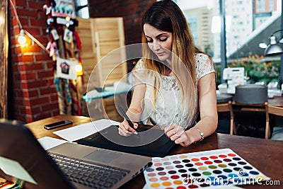 Portrait of young graphic designer working on new project using graphics tablet and laptop sitting in modern office Stock Photo