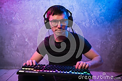 Portrait of the young handsome pro gamer sitting on the floor with keyboard in neon colored room Stock Photo