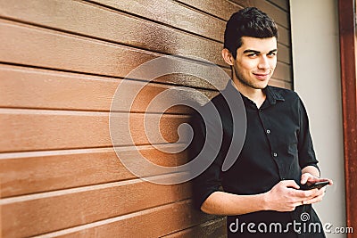 Portrait of young handsome Turkish male model. Mediterranean race brunette in black shirt is using a hand phone of a Stock Photo