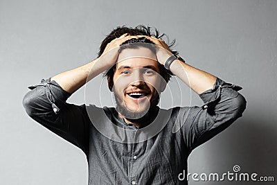 Portrait of young happy bearded guy with disheveled hair. Hold head with hands. Grey background. Stock Photo