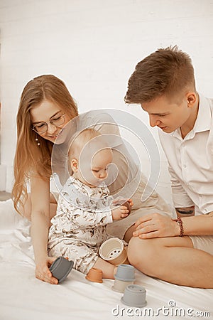 Portrait of young beautiful family sitting with little cute plump infant baby playing with modern pastel silicone bowls. Stock Photo