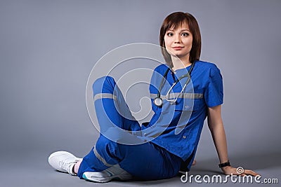 Portrait of a young, happy nurse during a working day. The girl on a gray background sits on the floor Stock Photo