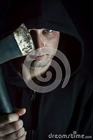 Portrait of a young hooded man with blue eyes who with an ax in his hand has a disturbing look - focus on the eye Stock Photo