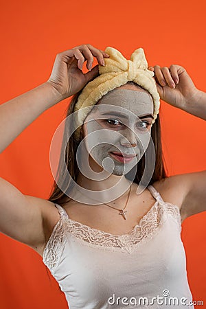 Portrait of young lady with green nourishing caly mask on face on orange Stock Photo