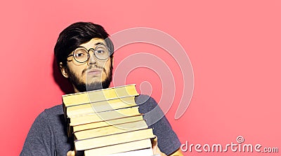 Portrait of young laughing man, holding bunch of books, wearing round eyeglasses on background of coral pink color. Stock Photo