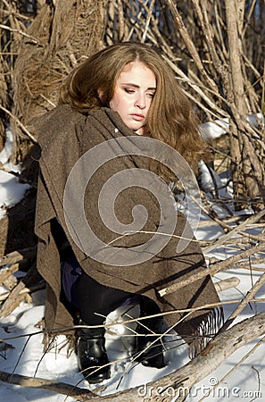 Portrait of young lonely girl sitting in winter snowy forest. Unhappy freezing woman. Stock Photo