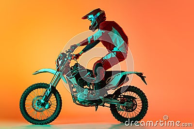 Portrait of young man, biker in full equipments riding motorbike isolated over orange studio background in neon light Stock Photo