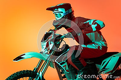 Portrait of young man, biker in full equipments riding motorbike isolated over orange studio background in neon light Stock Photo