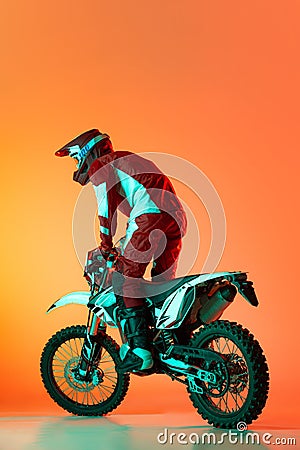 Portrait of young man, biker in full equipments riding motorbike isolated over orange studio background in neon light Stock Photo