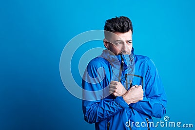 Portrait of a young man with blue anorak in a studio, feeling cold. Copy space. Stock Photo