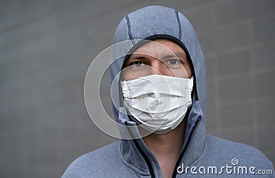 Portrait of young man in gray hoodie and home made cotton face mouth virus mask, gray wall in background Stock Photo