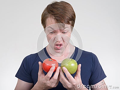 Portrait of young man looking disgusted while holding tomato and apple Stock Photo