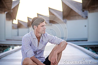 Portrait of young man model posing in expensive clothes sitting near water bungalows at the tropical island luxury resort Stock Photo