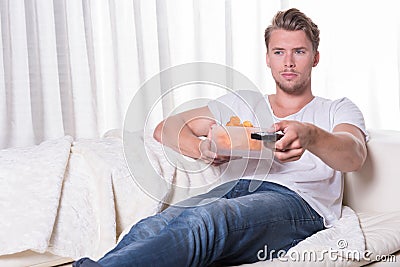 Portrait young man sitting on couch and eating chips and zapping Stock Photo