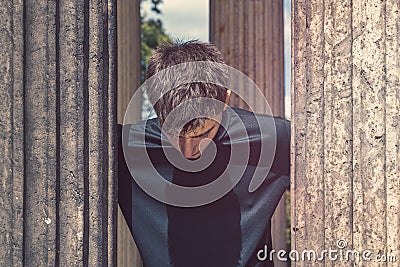 Young man standing between antique columns and looking down Stock Photo