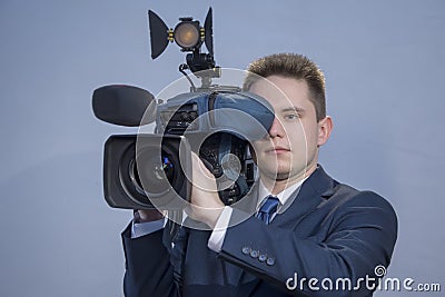 Portrait of a young man in a suit, who stands holding a TV camera on his shoulder on a light background. The operator works with Stock Photo