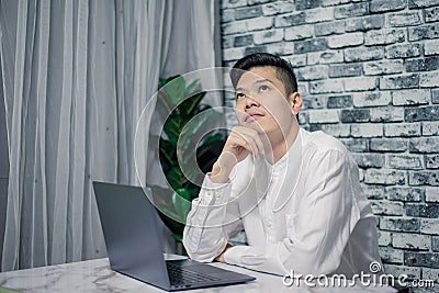 Portrait of young man thinking while serious working at home with laptop on desk Stock Photo