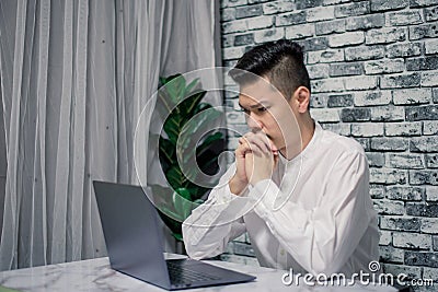 Portrait of young man thinking while serious working at home with laptop on desk Stock Photo