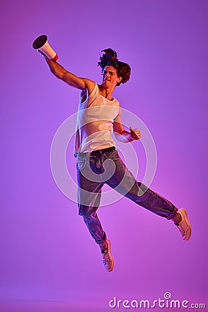 Portrait of young man in white T-shirt, singlet posing in a jump over purple background in neon light Stock Photo