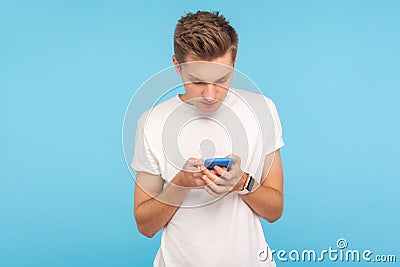 Portrait of young man in white t-shirt using cellphone with focused serious expression, addicted to mobile communication Stock Photo