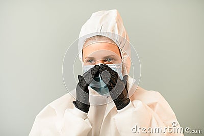 Portrait of young medic woman in white protective suit with hood which corrects surgical mask on face. Stock Photo