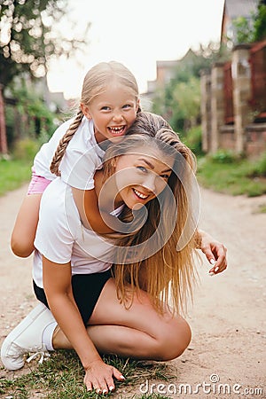 Portrait of young mother carrying her daughter on her back outdoor. Happy chilhood Stock Photo