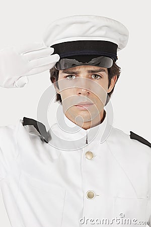 Portrait of young navy officer saluting against gray background Stock Photo
