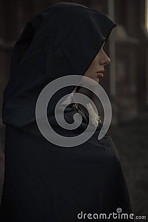 Portrait of young nun in black cassock and hooded cloak with cross. Stock Photo