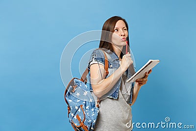 Portrait of young pensive woman student in denim clothes with backpack taking exam thinking about test holding notebook Stock Photo